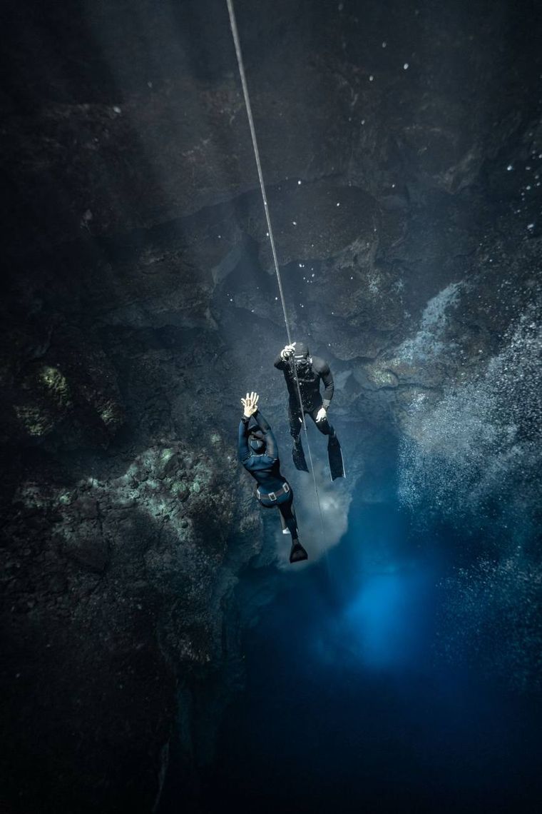 Two freedivers descending past sun beams in a cenote