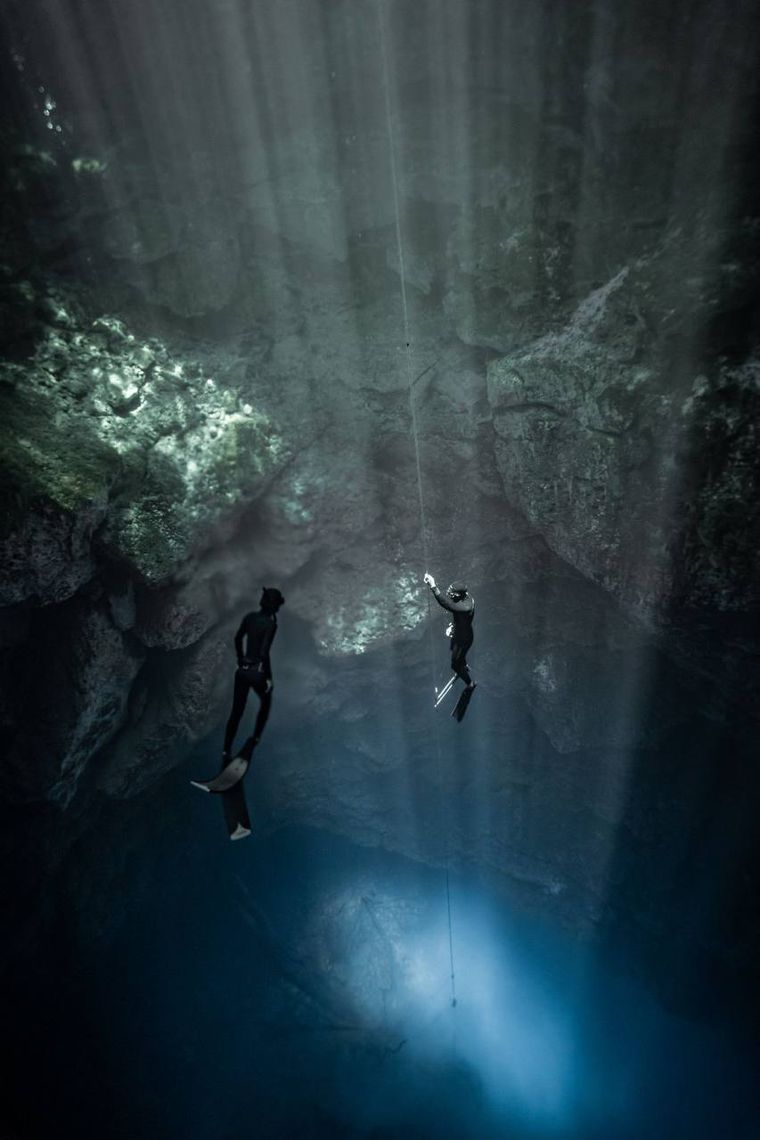 Freedivers in a cave passage with god rays
