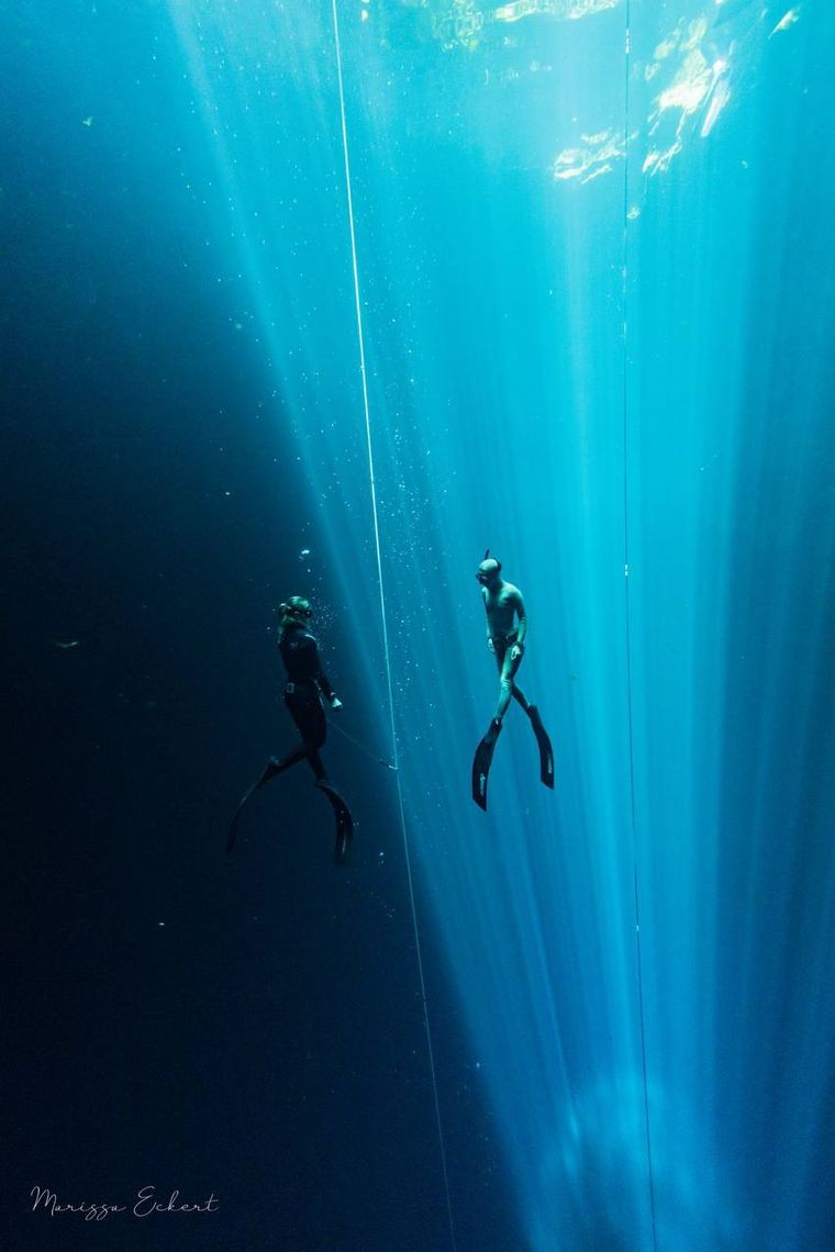 Two freedivers in light beams inside a cenote