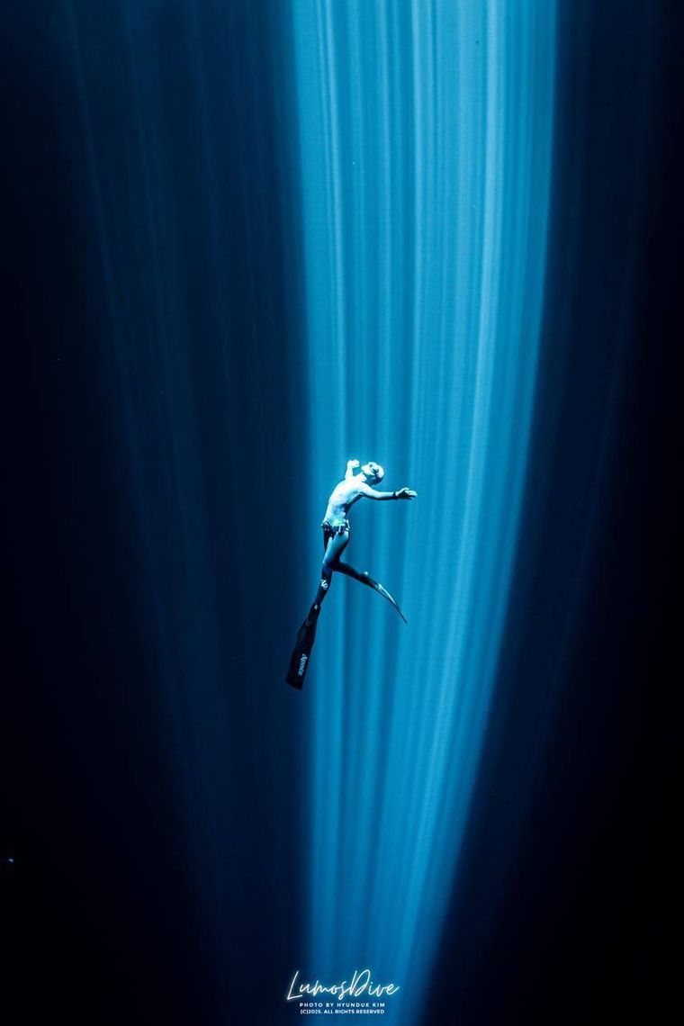 Freediver ascending through a shaft of light in a cenote