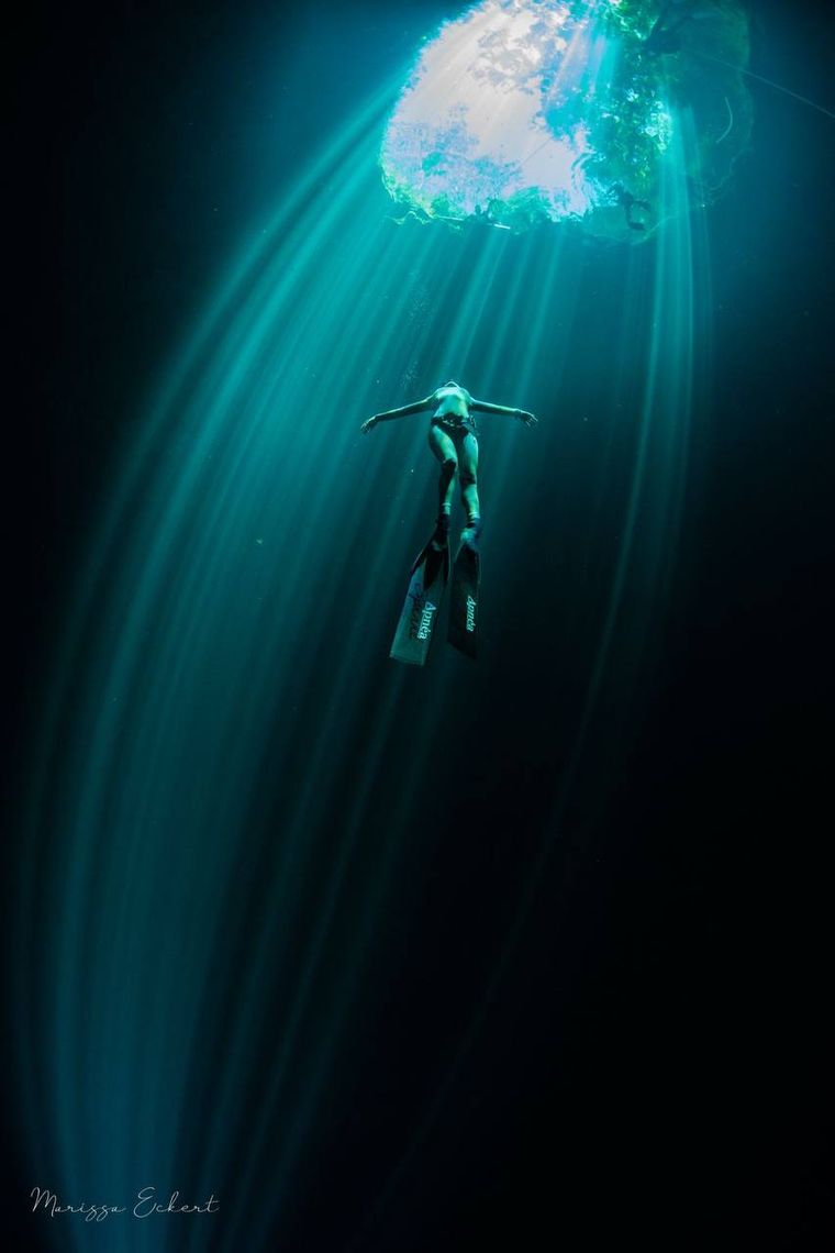 Freediver under a cenote dome with light rays